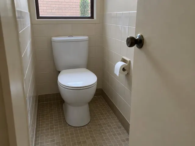 Clean white toilet in a tiled bathroom with a small window and open door in Canley Vale