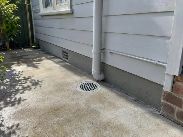 Outdoor gully grate beside weatherboard house and concrete path in Fairfield